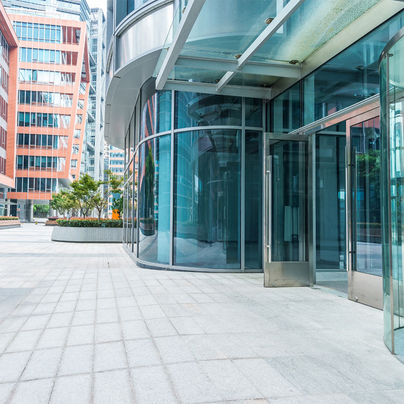The entrance to a blue glass building in a plaza.