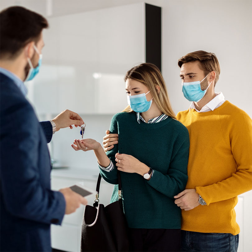 A man and woman wearing masks are handed a set of keys by another man wearing a mask.