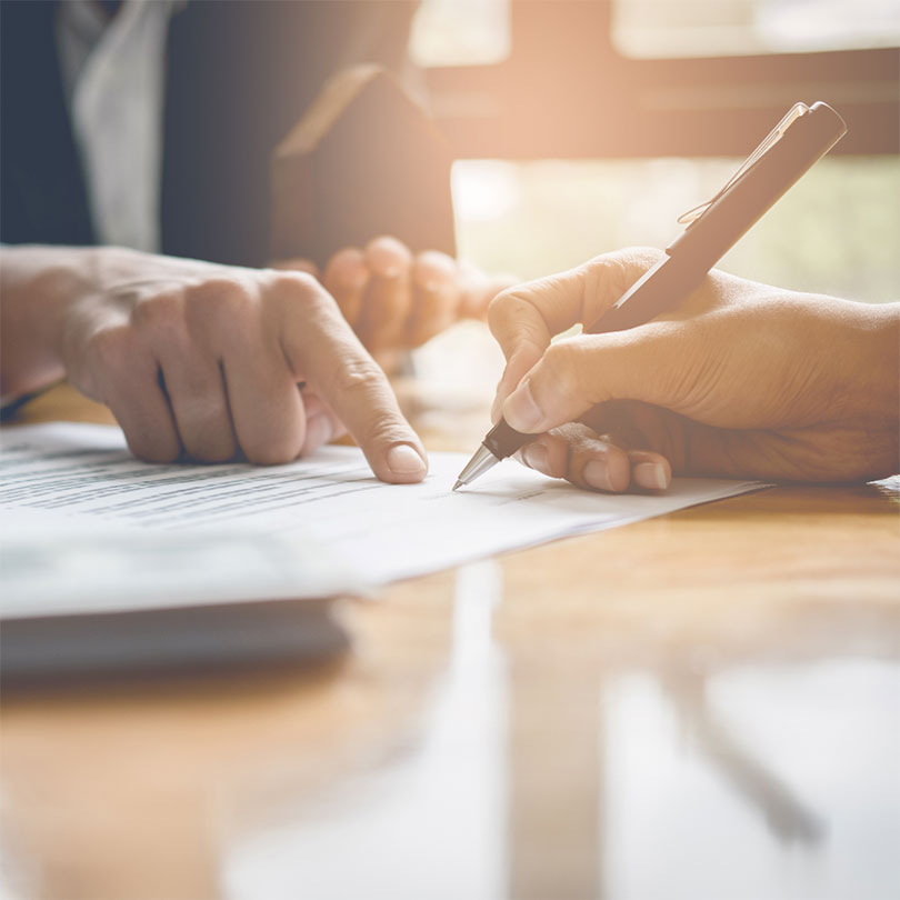 A person points out to another person holding a pen where to sign a document.
